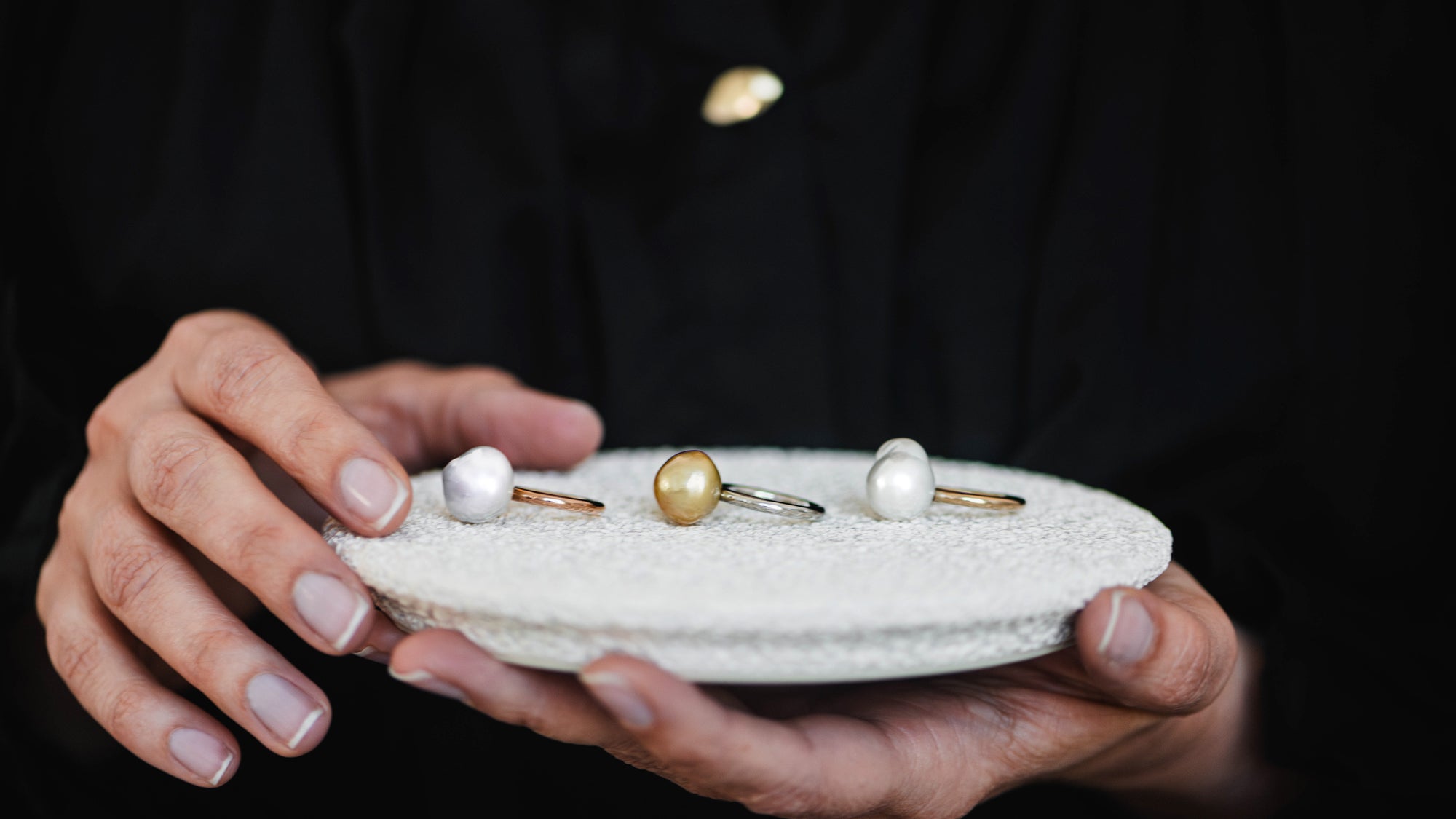 Three Ayla Pearl Rings in yellow and white gold featuring hand-selected unique baroque white and golden South Sea pearls rest on a white textured ceramic jewellery dish.