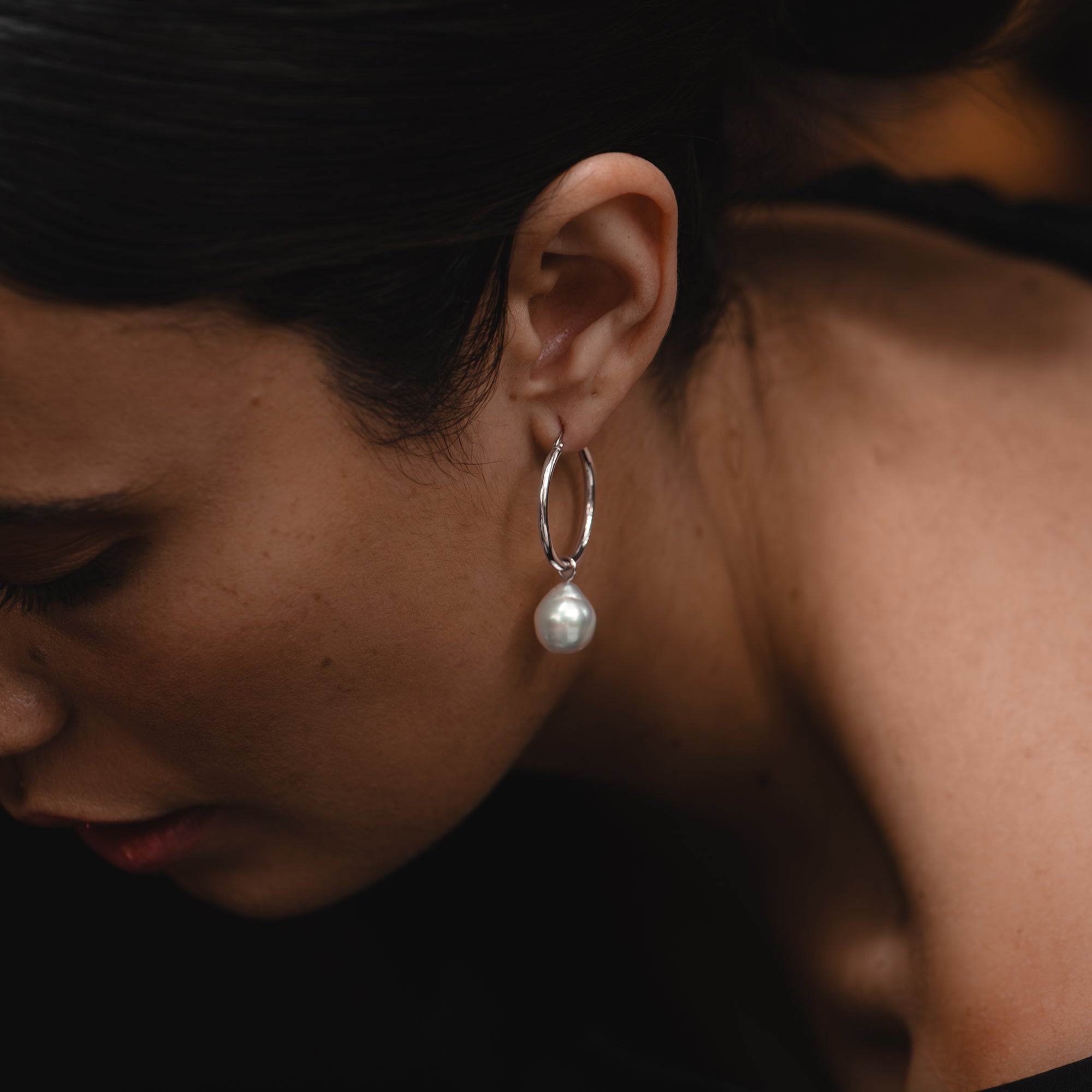 Small white gold hoop earrings with detachable baroque white South Sea pearls, worn by a woman