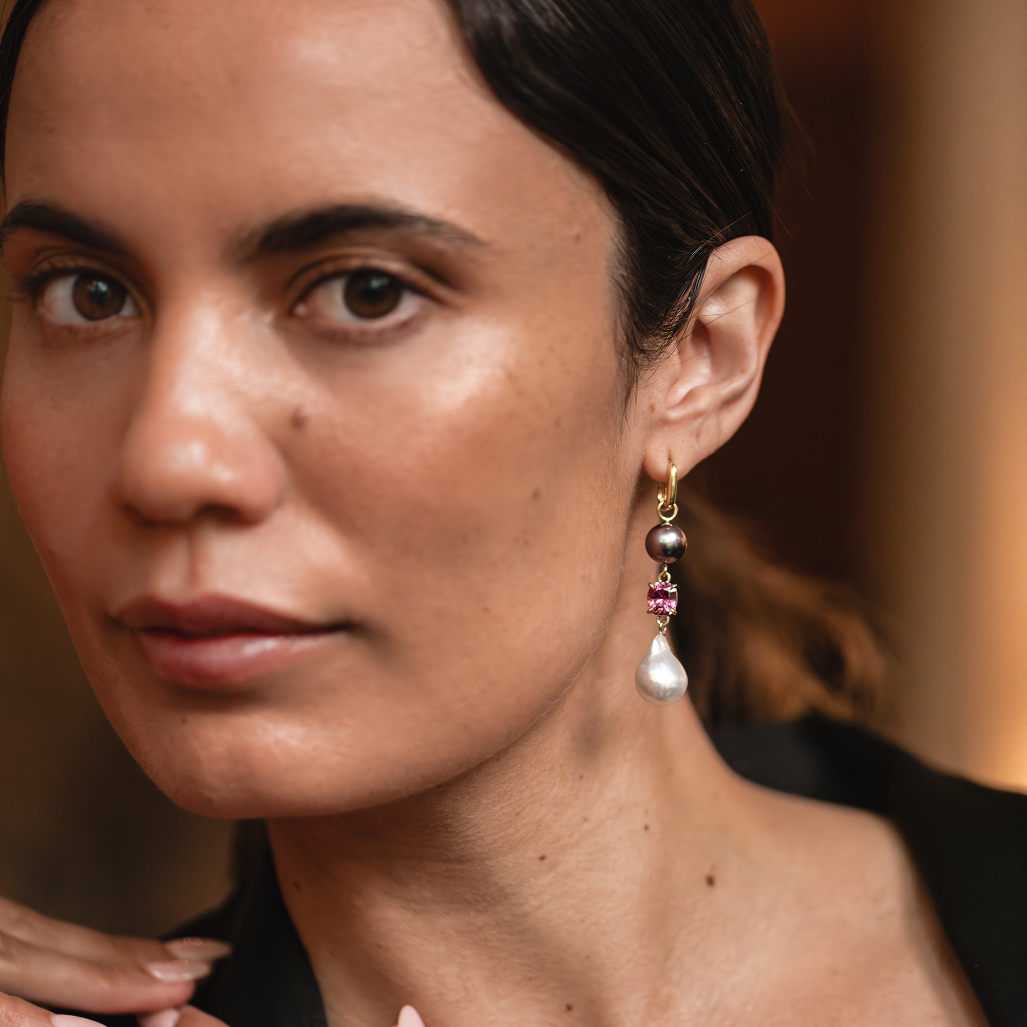 Yellow gold huggie earring with a pink garnet, a purple Tahitian pearl, and a white South Sea pearl worn on a woman's ear.