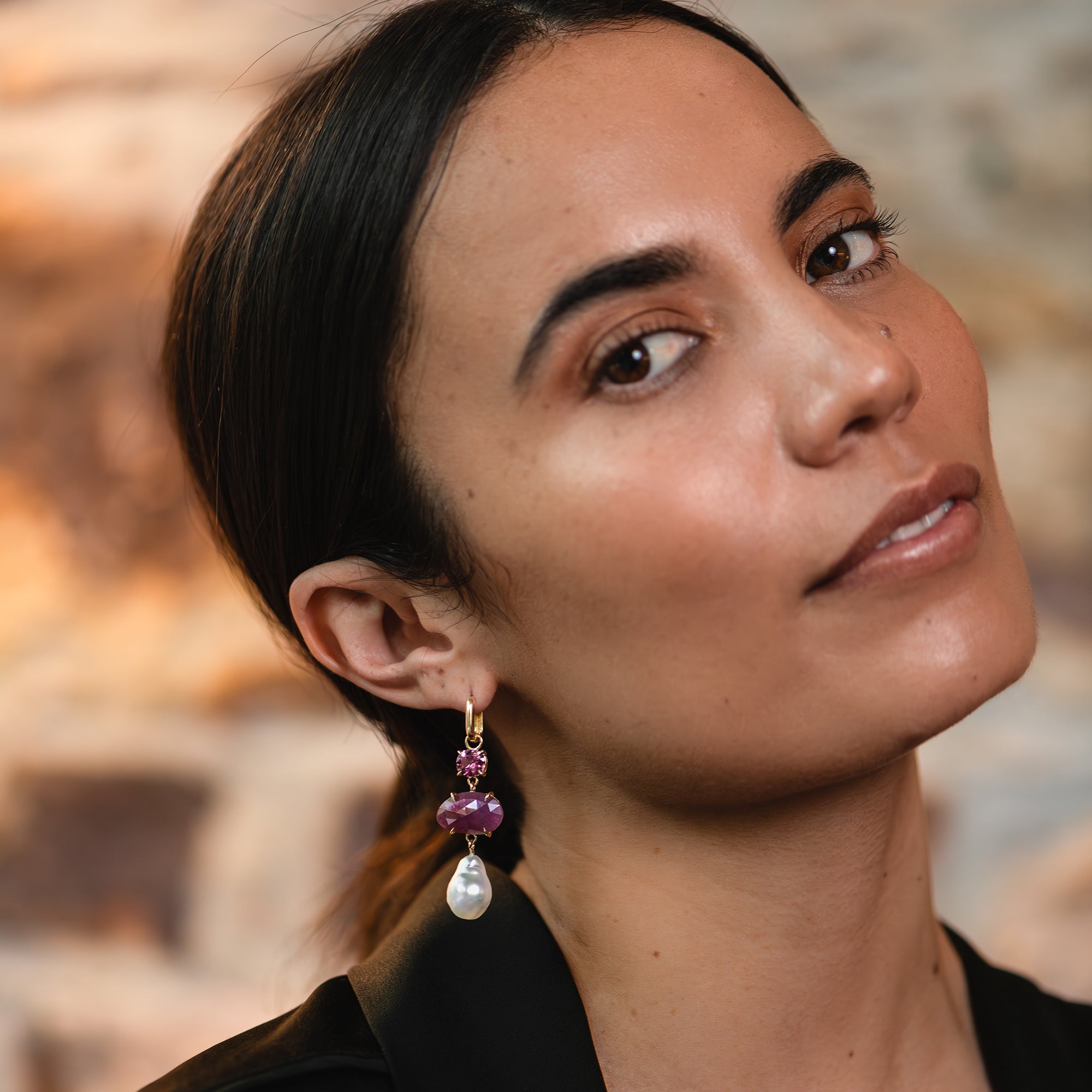 Yellow gold huggie earring with ruby, pink garnet, and a white South Sea pearl worn on a woman's ear.
