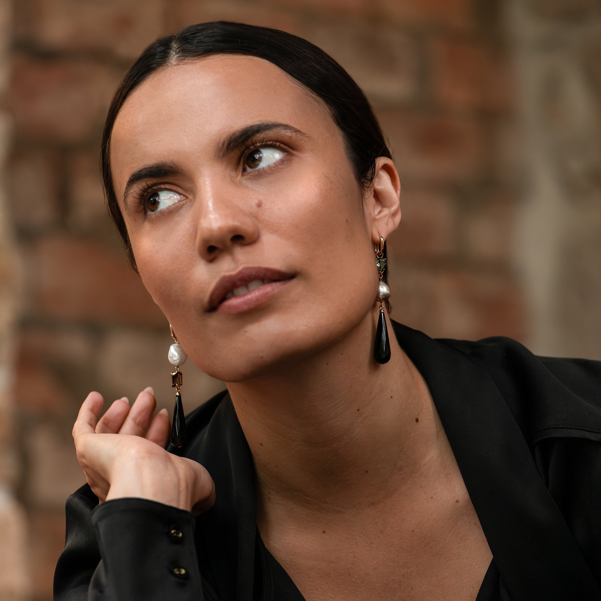 A pair of rose gold tourmaline, South Sea pearl, and onyx briolette drop huggie earrings worn by a woman.
