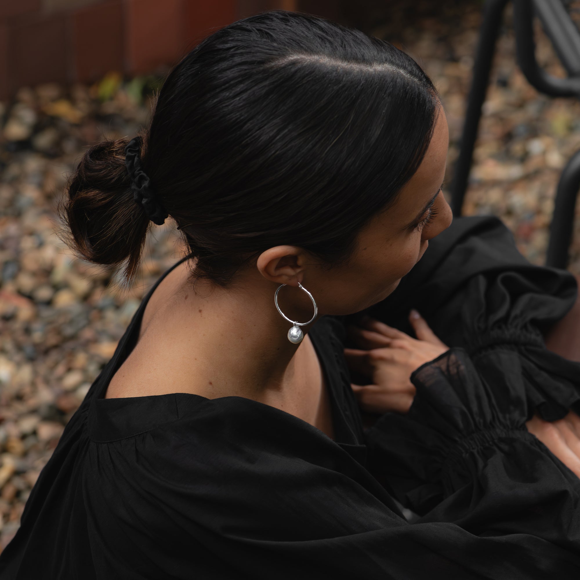 Medium white gold hoop earrings with detachable baroque white South Sea pearls, worn by a woman with her arms crossed, looking down.