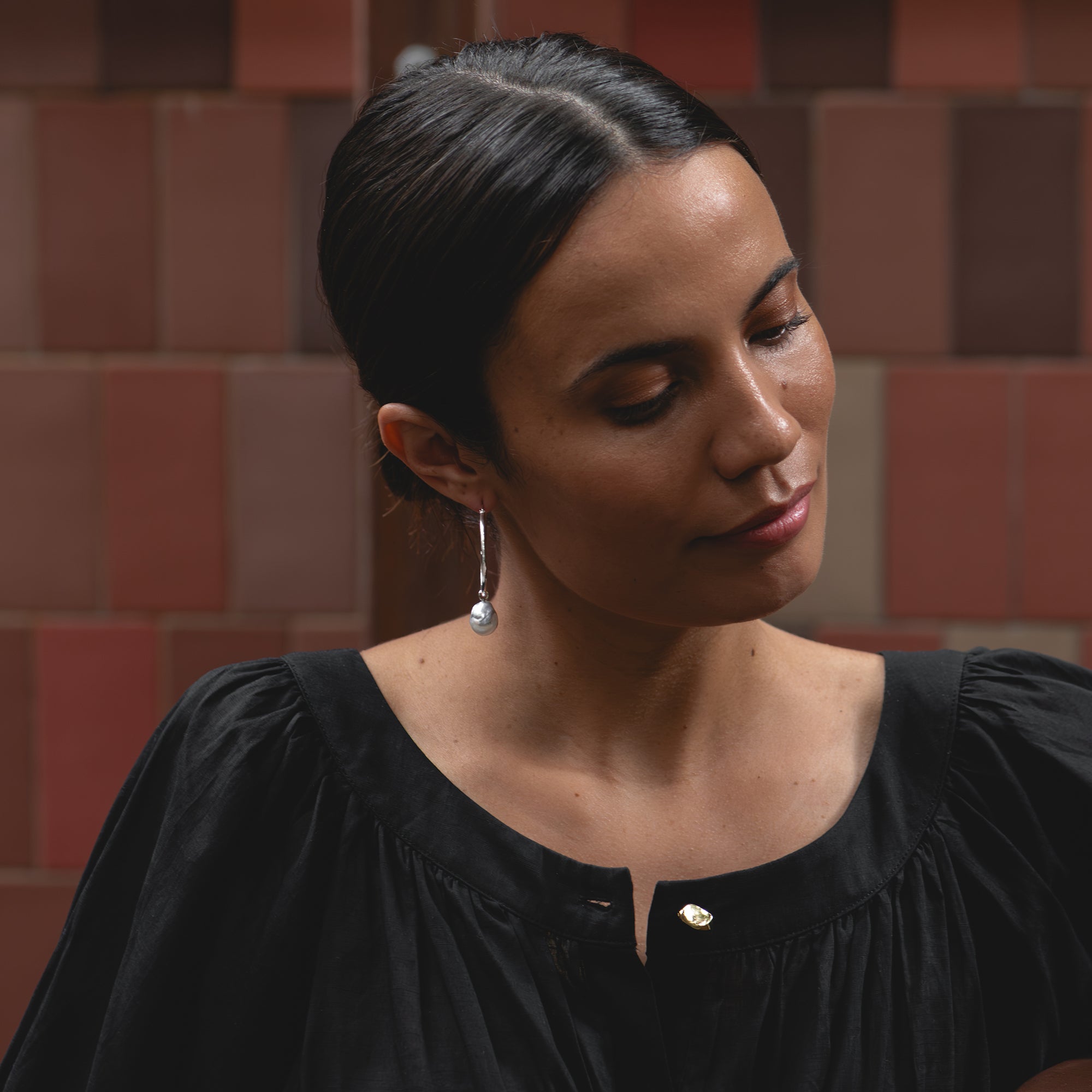 Medium white gold hoop earrings with detachable baroque white South Sea pearls, worn by a woman sitting outdoors in a boutique hotel courtyard.