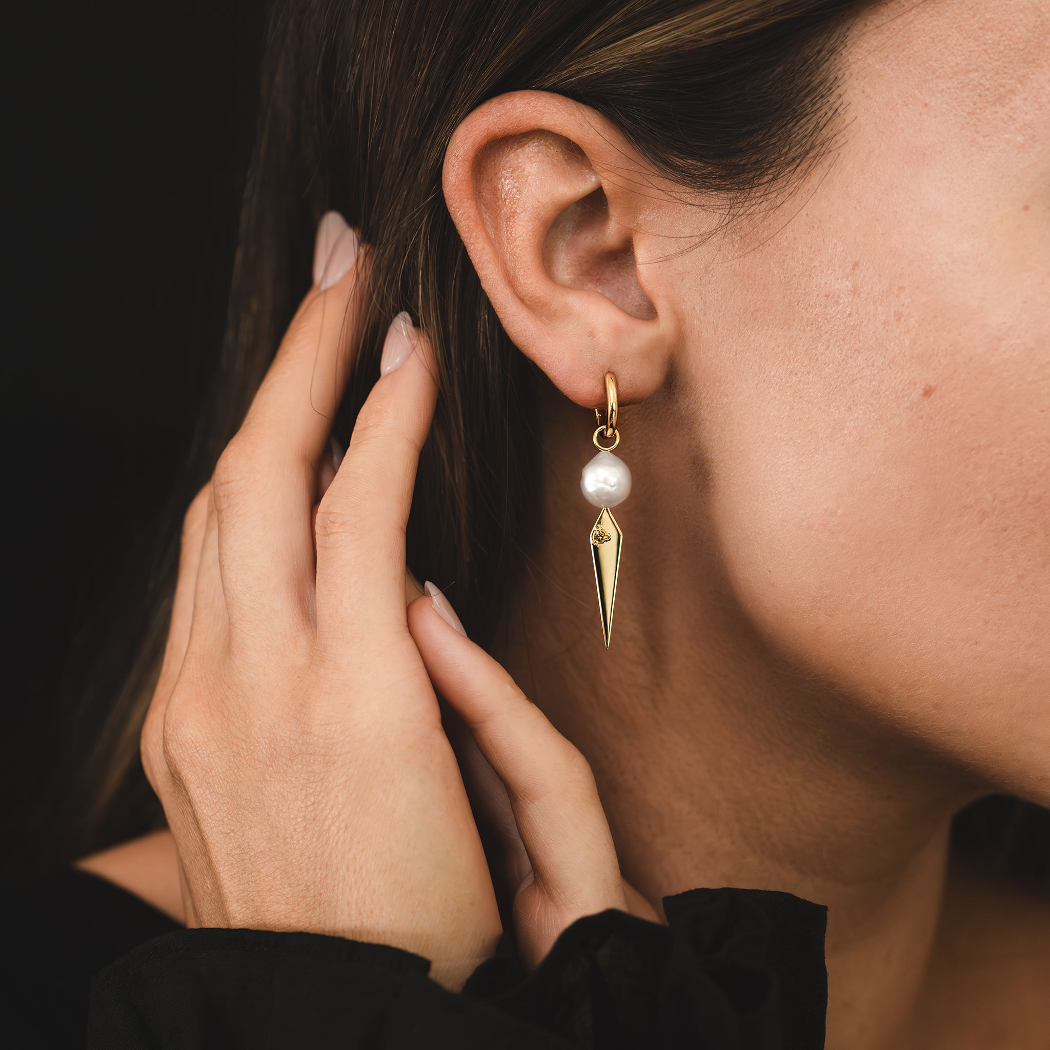 A single huggie earring featuring a white baroque South Sea pearl and yellow gold kite shaped drop set with an earthy coloured Australian champagne diamond is being worn in a woman's ear lobe.