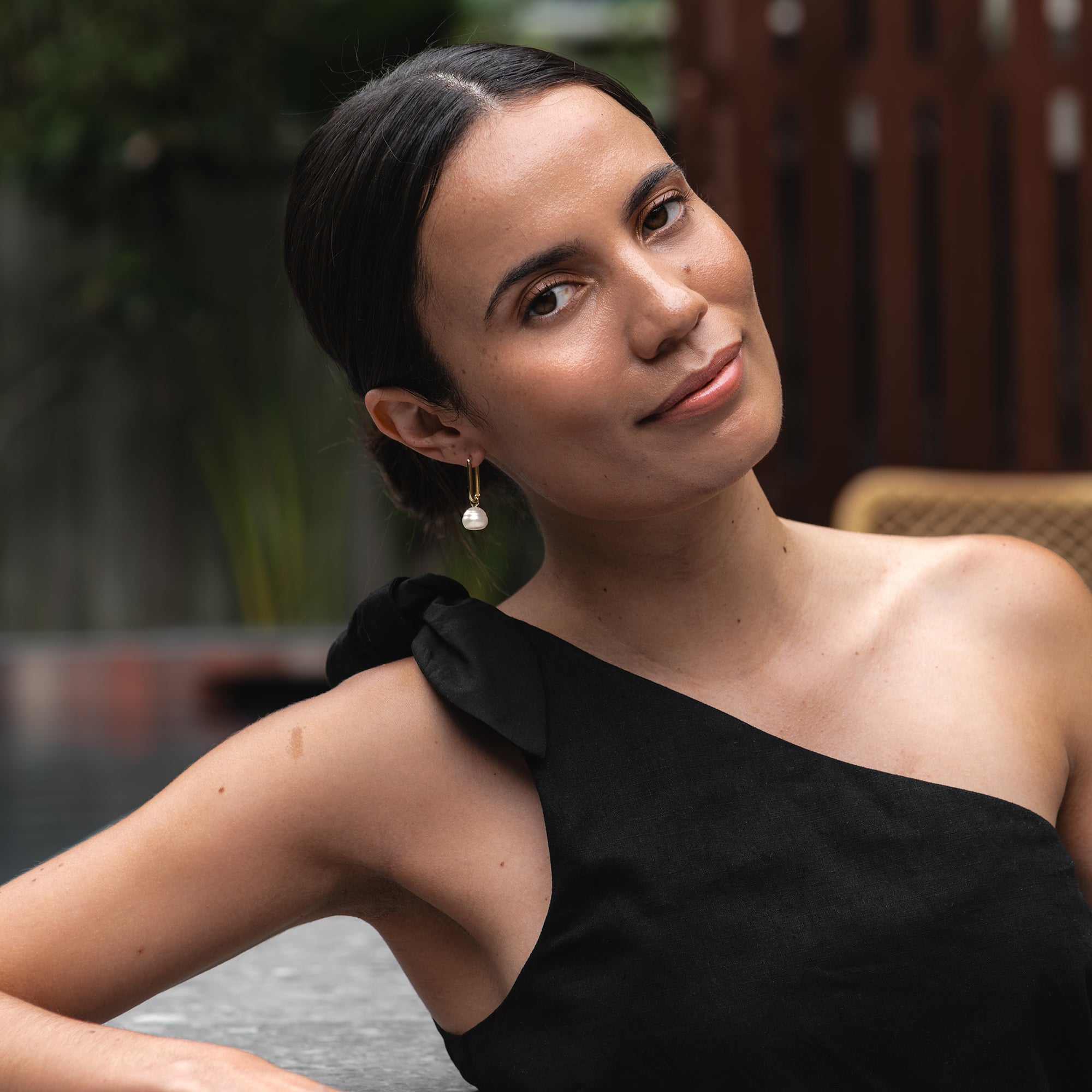 Yellow gold paperclip hoop earring with a circle white South Sea pearl, worn by a woman lounging by a boutique hotel pool.
