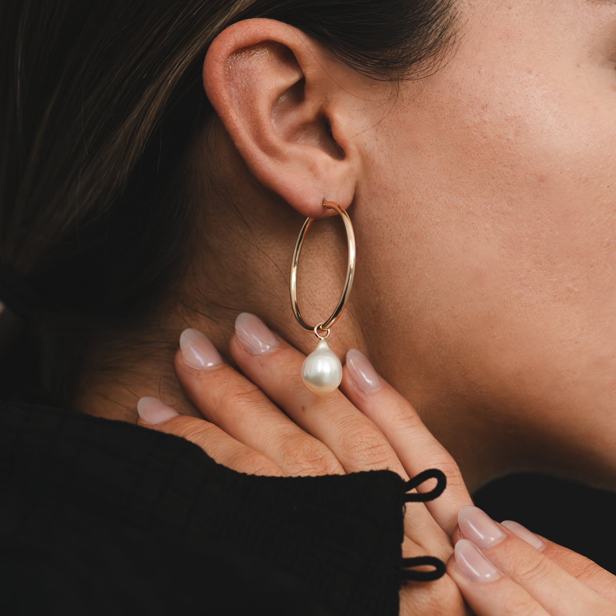 Hand selected unique baroque white and golden South Sea pearls, in a hand crafted yellow gold detachable setting, on large yellow gold high polish hoop earrings, worn by a woman.