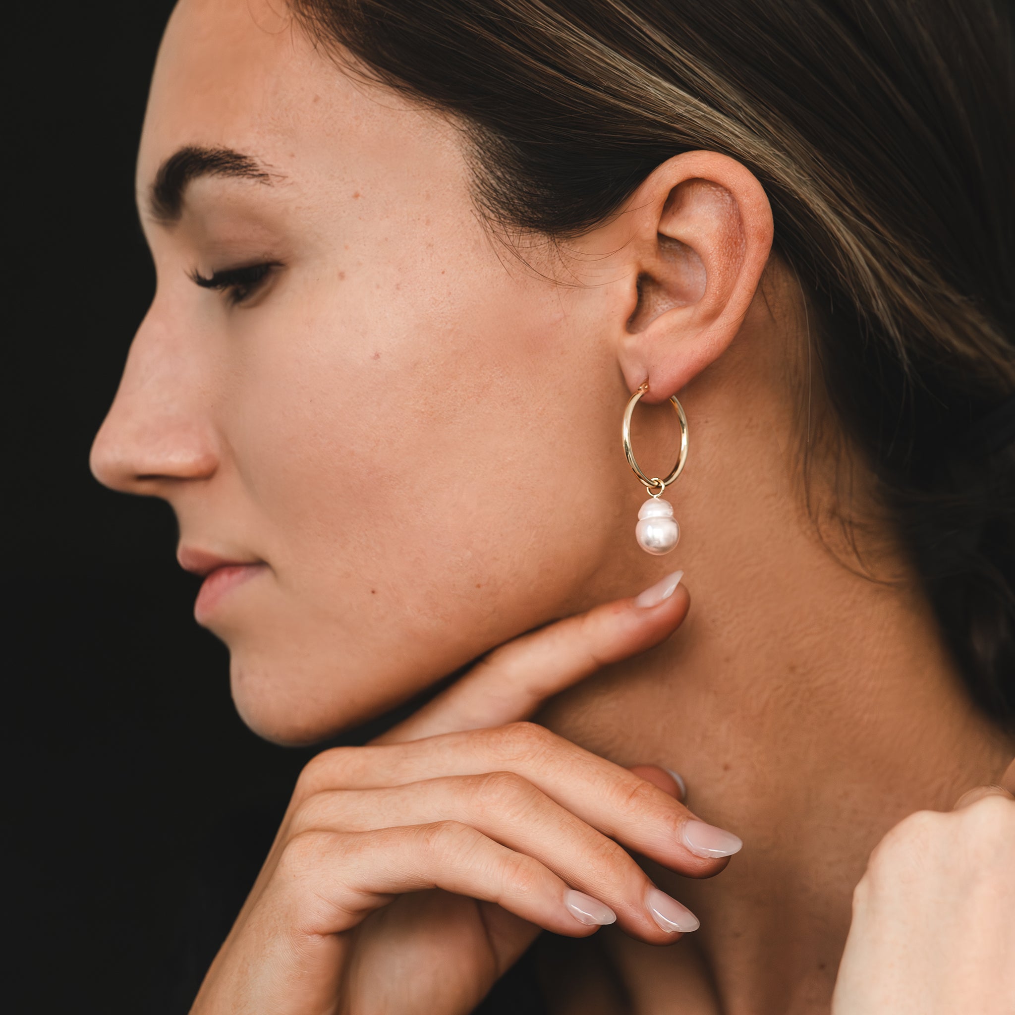 Hand selected unique baroque white South Sea pearls, in a hand crafted yellow gold detachable setting, on small yellow gold high polish hoop earrings, worn by a woman.