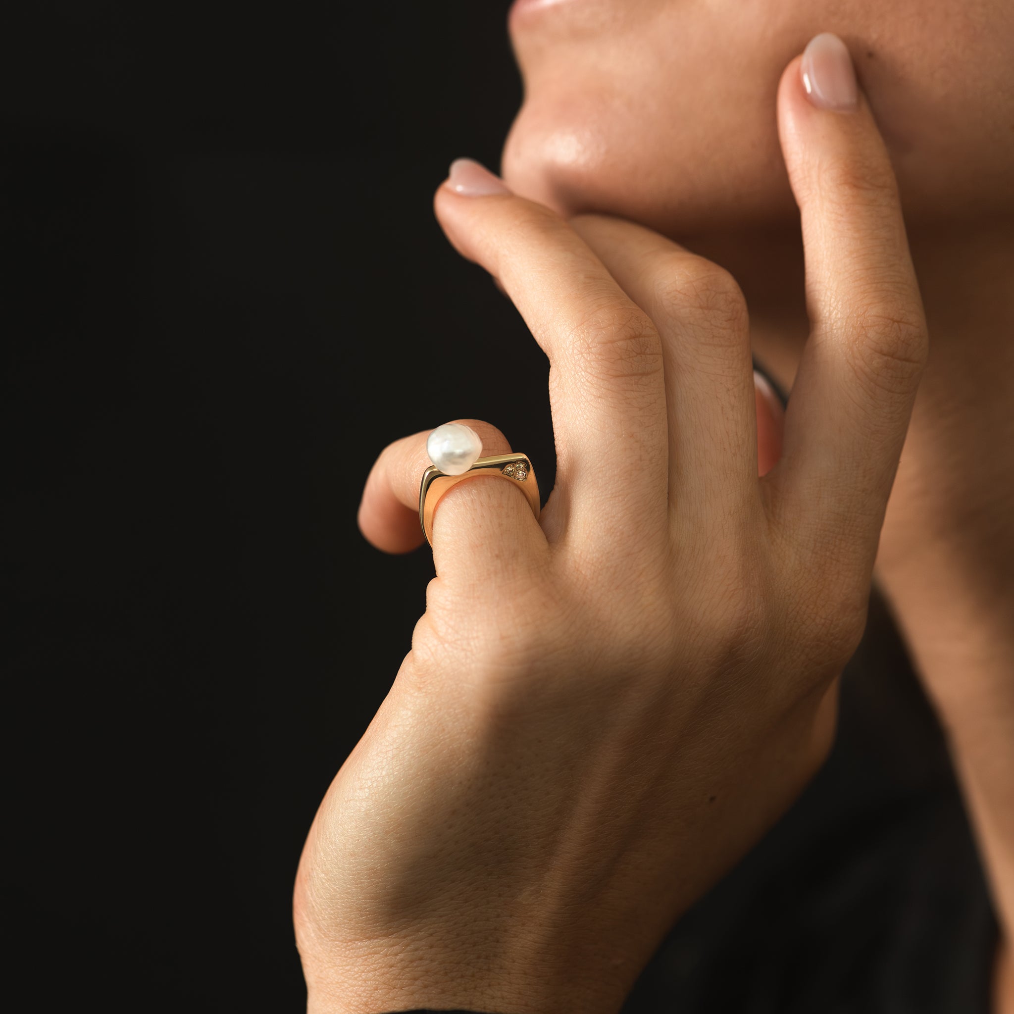 A yellow gold ring featuring a hand selected unique baroque white South Sea pearl and a trio of Australian champagne diamonds in earthy coloured tones is being worn on a woman&#39;s pinkie finger.