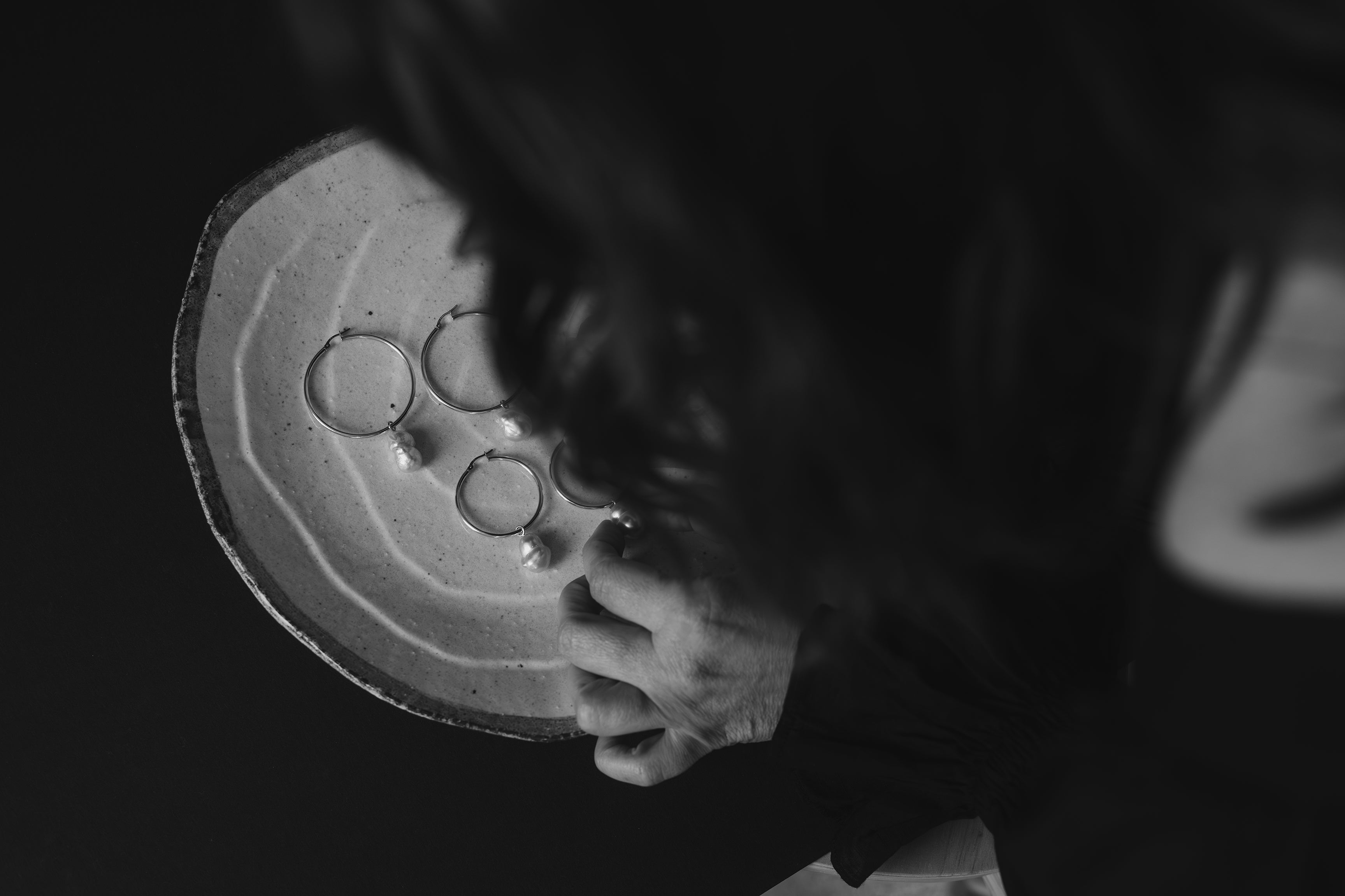 A view from overhead looking down at Rachael arranging Ayla pearl hoop earrings on a cream coloured textured ceramic platter.